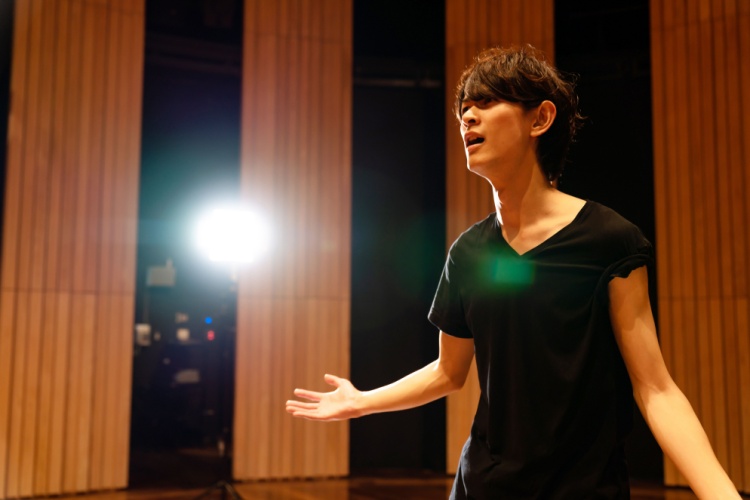 a young actor stands alone on the stage performing a monologue